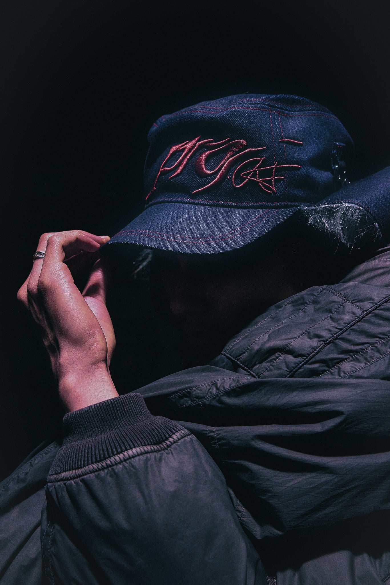 Person wearing the ANTIFRAGILE Military Hat with fur flaps showcasing the custom maroon red 3D puff print embroidery. He holds the hat's short brim.