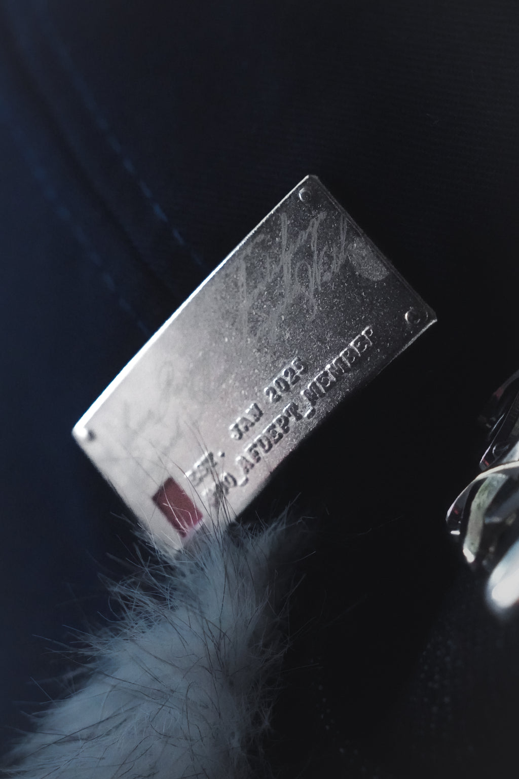Metallic rectangular identifier tag with embossed text on the Antifragile fitted navy blue cap.