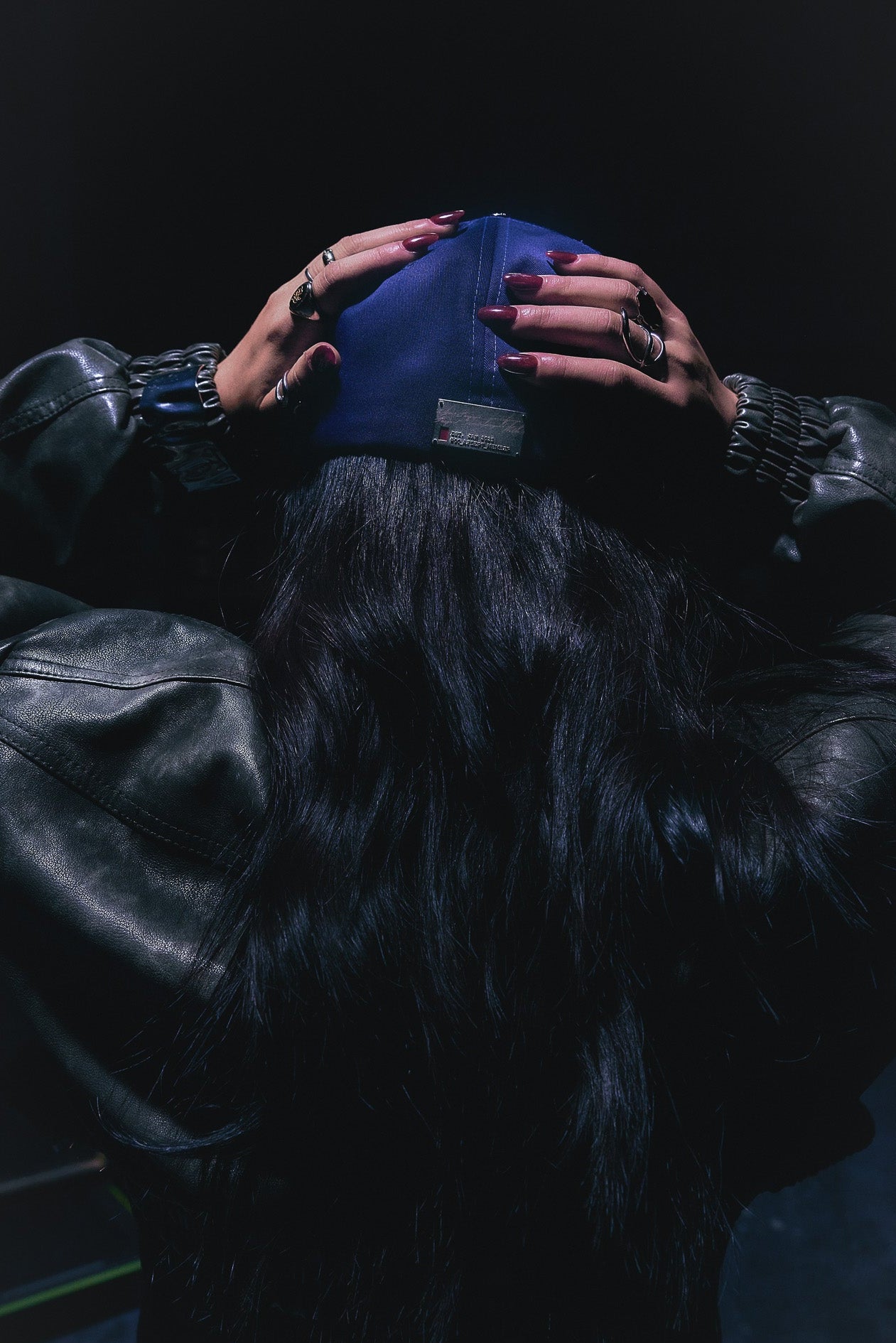 Person wearing the ANTIFRAGILE Fitted Navy Blue Hat with their hands on the back of the hat. The custom 3D embossed metal tag identifier is pictured at the back of the hat.