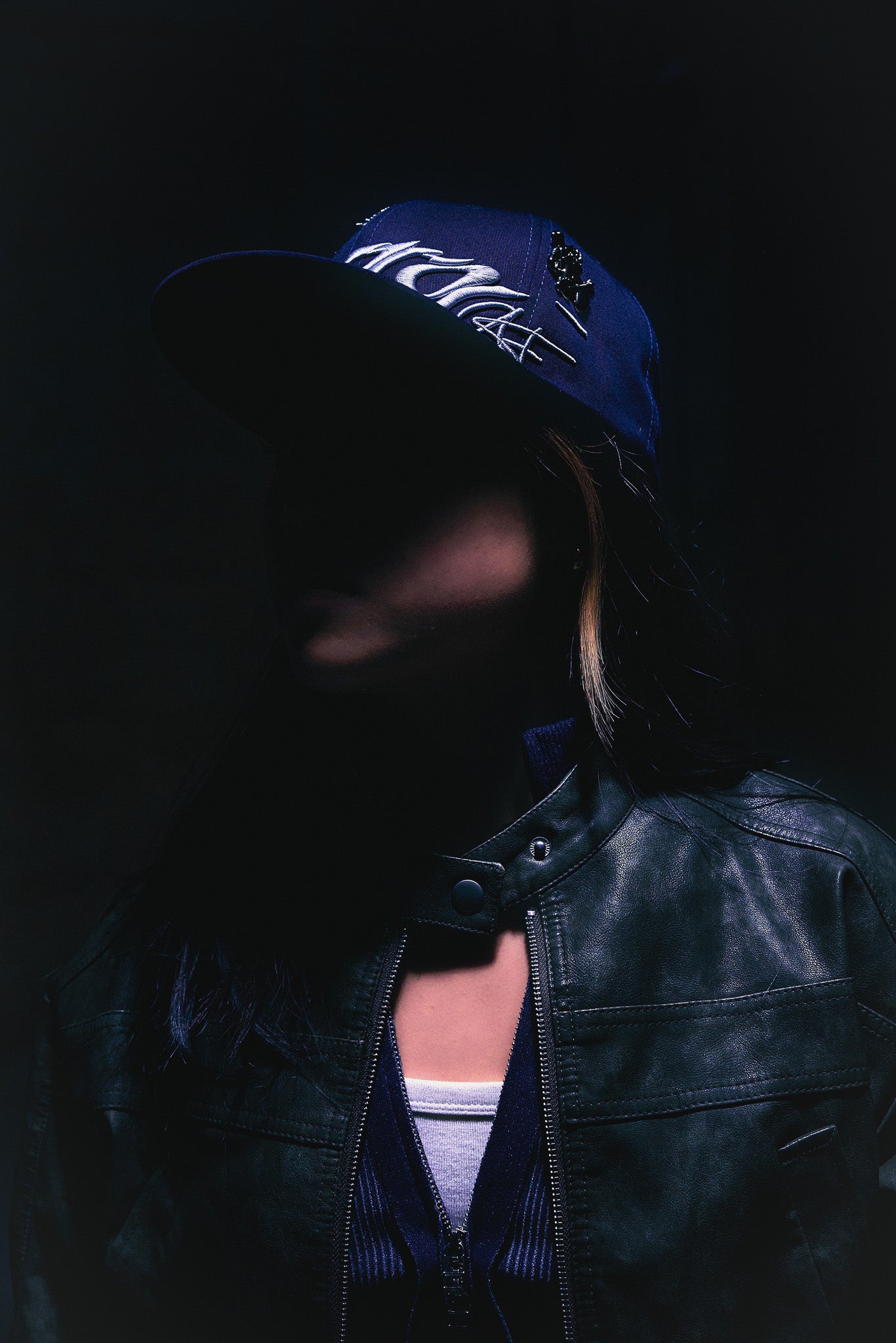 A creative seen wearing the ANTIFRAGILE Navy Blue Fitted Cap showcasing the 3D puff print embroidery as it catches the reflection from the light above.