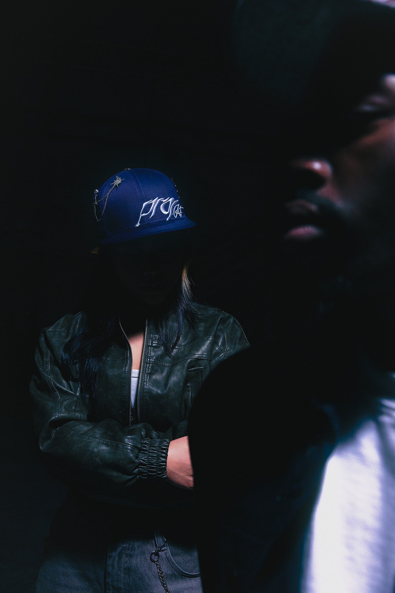 Person wearing the ANTIFRAGILE Fitted Navy Blue Hat, arms crossed, looking down. 