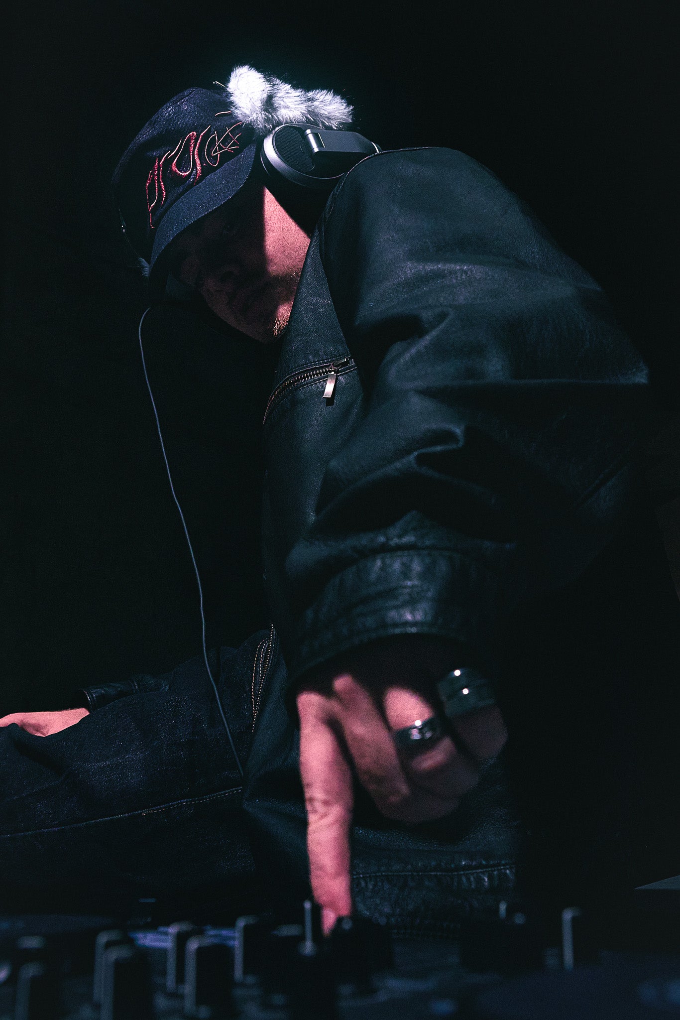 A creative producer and DJ interacting with a DJ deck. They are seen wearing the ANTIFRAGILE Military Fur Cap with their USB hooked onto the custom metal clasp. 