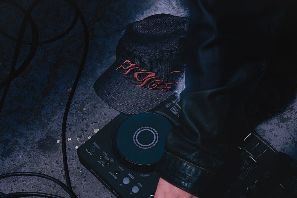 The ANTIFRAGILE Military Fur Cap is propped against a DJ deck with loose cables running around the concrete floor. 
