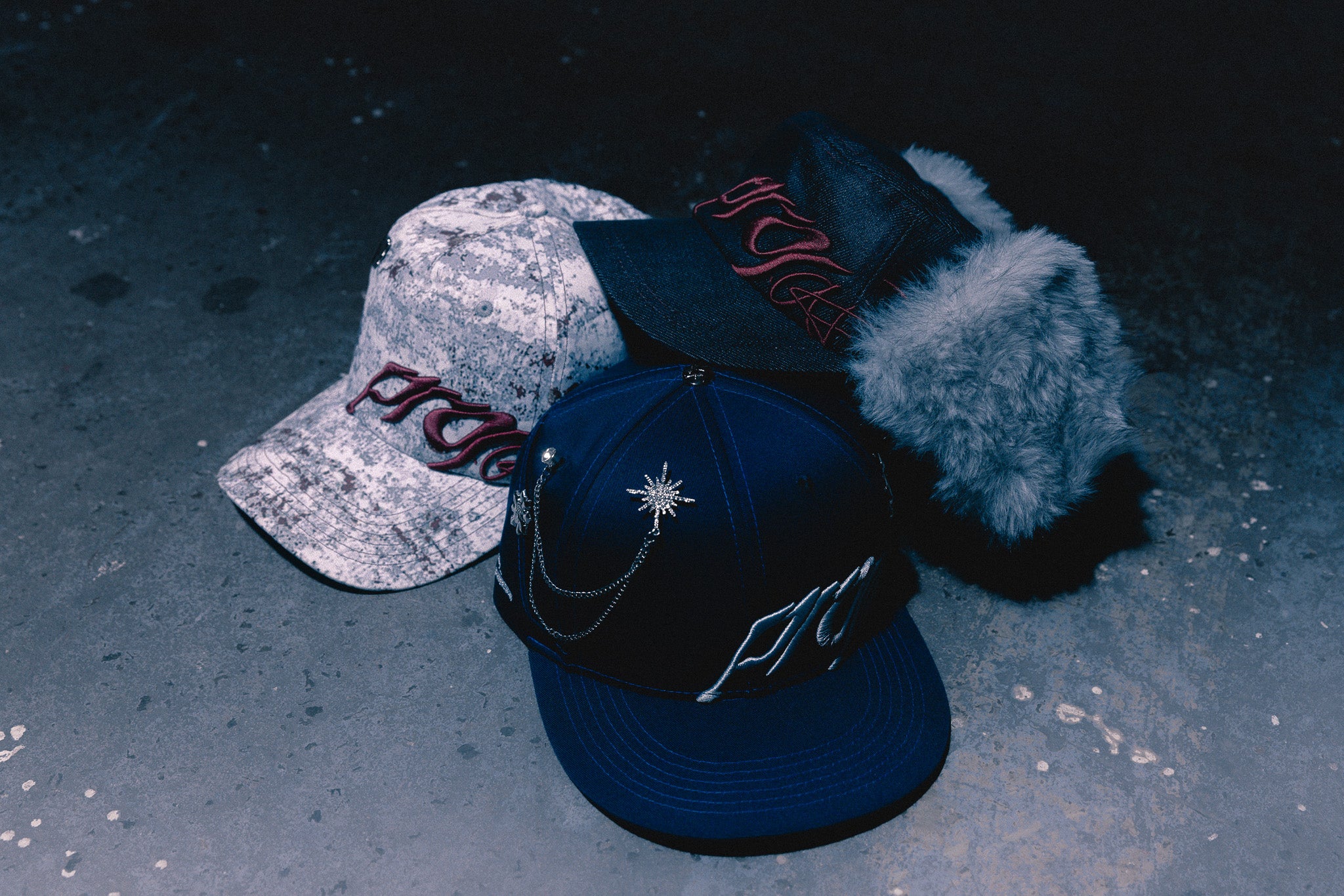 Three ANTIFRAGILE hats with different designs and colors on a textured surface. It showcases the unique designs and pins created with the AFDEPT.